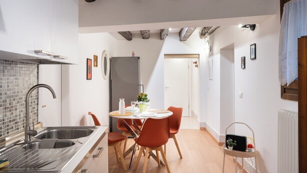 Una cuina moderna amb un rentaplat, un frigorífic i una zona de menjador amb caires i taula.