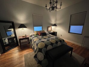 Ein Schlafzimmer mit einem Bett, Nachttischen, einem Spiegel, einer Chandelieber und einem Fenster.