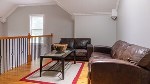 Ein Wohnzimmer mit einem braunen Ledersofa, einem Glastisch mit einem gewebten Korb, einem roten und weißen Teppich und einer Holztreppe mit Geländer.