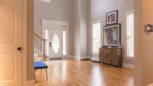 Ein geräumiger Raum mit Holzdielen, einer Treppe, einer Tür mit Glasfenster und einem Schrank mit gerahmten Kunstwerken.
