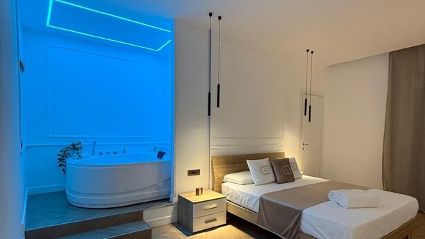 A modern bedroom with a built-in bathtub, a bed with a wooden headboard, and a minimalist design. - Anthony Emanuele Fuoco (Torre del Greco)