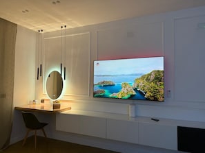 Una sala de estar moderna con un televisor de pantalla plana montado en la pared, un escritorio de madera con un espejo y una silla negra.