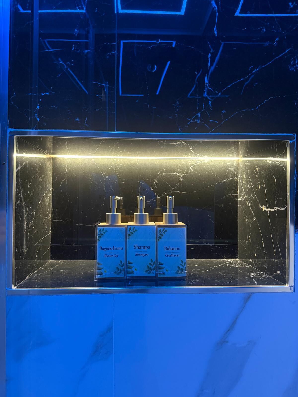 Un baño con encimera de mármol y tres productos Bagnoschioma: gel de ducha, champú y acondicionador.