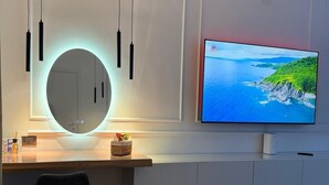A modern living room with a TV, a round mirror, pendant lights, and a wooden floor. - Anthony Emanuele Fuoco (Torre del Greco)