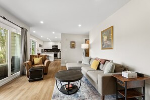 A modern living room with a sofa, armchair, and coffee table, a kitchen in the background, and a balcony with a view. - Edwards Condo - near Shaw Center & Beaver Creek (Edwards)