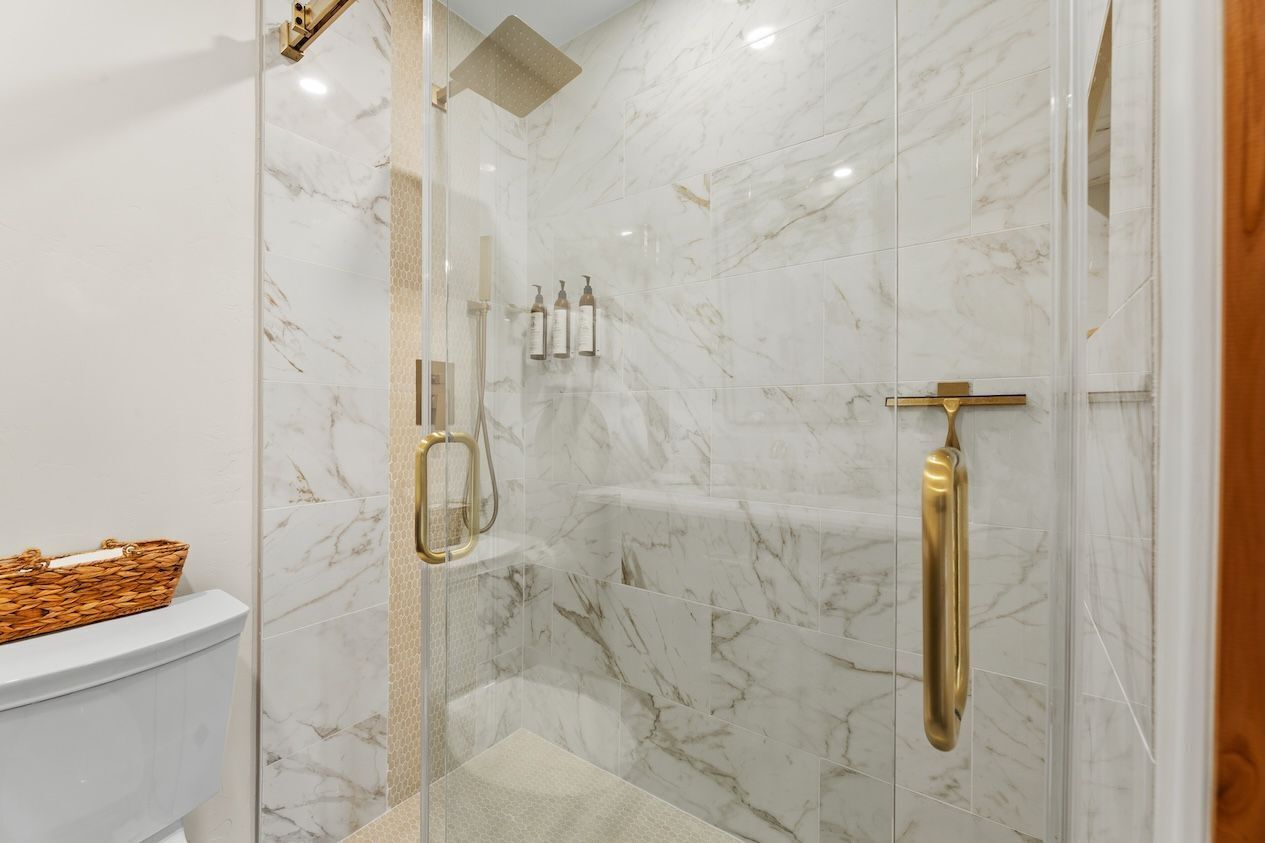 Ein Badezimmer mit einer gläsernen Duschkabine, Marmorwänden und einem WC mit Korbwannen.