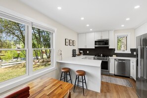A modern kitchen with white cabinetry, stainless steel appliances, and a large window overlooking a garden. - Edwards Condo - near Shaw Center & Beaver Creek (Edwards)