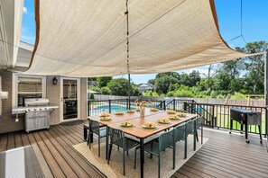 Een overdekt terras buiten, met een barbecue, eettafel en stoelen.