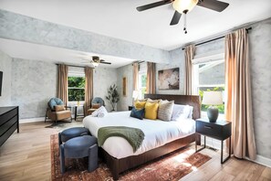Een slaapkamer met een groot bed, plafondventilator en uitzicht op groen.