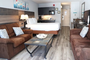 Ein Hotelzimmer mit einem Bett, zwei Sofas, einem Couchtisch, einem Schreibtisch, einem Fernseher und einer Küchenzeile.