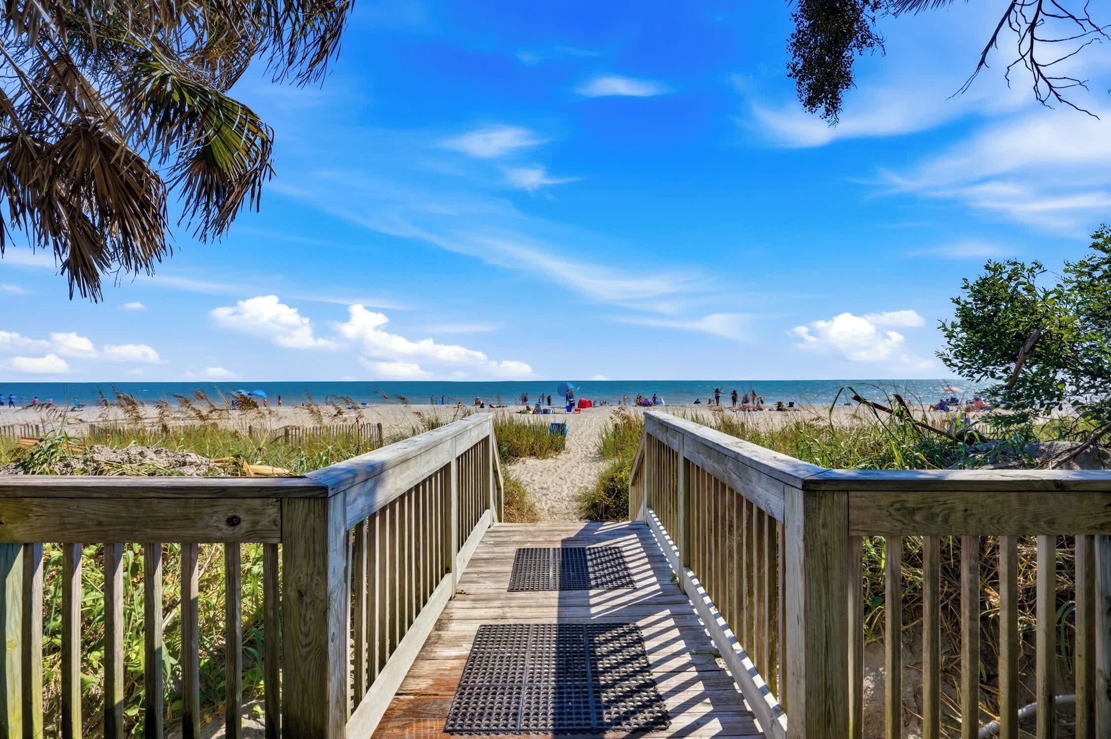 A wooden boardwalk leading to a beach with a clear sky.