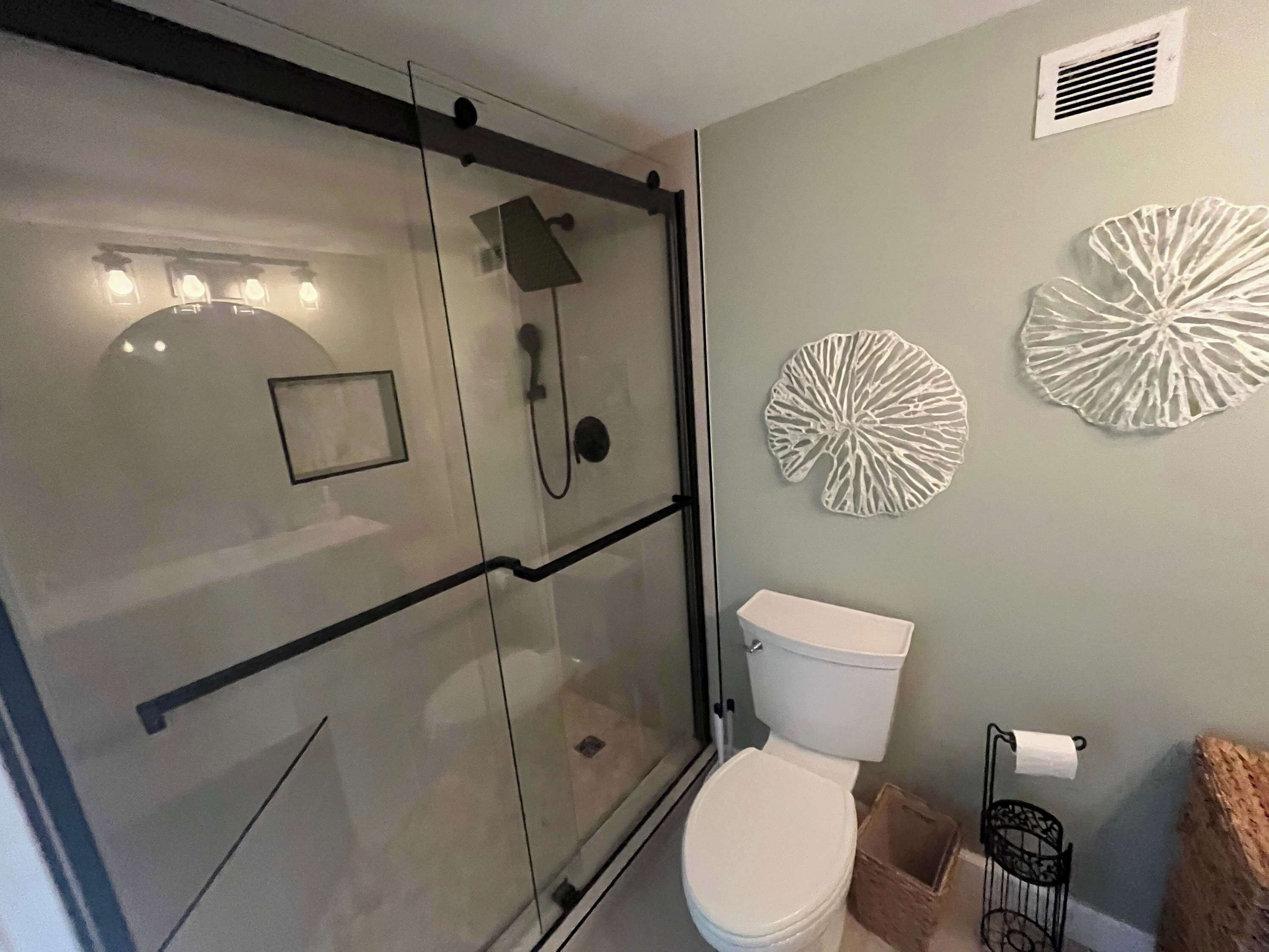 A modern bathroom with a glass shower enclosure, a toilet, and decorative wall art.