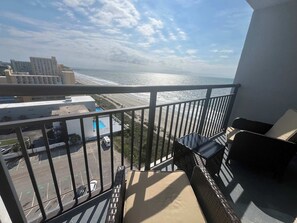 Ein Balkon mit Blick auf Strand und Meer, ein Parkplatz sowie ein Gebäude im Hintergrund.