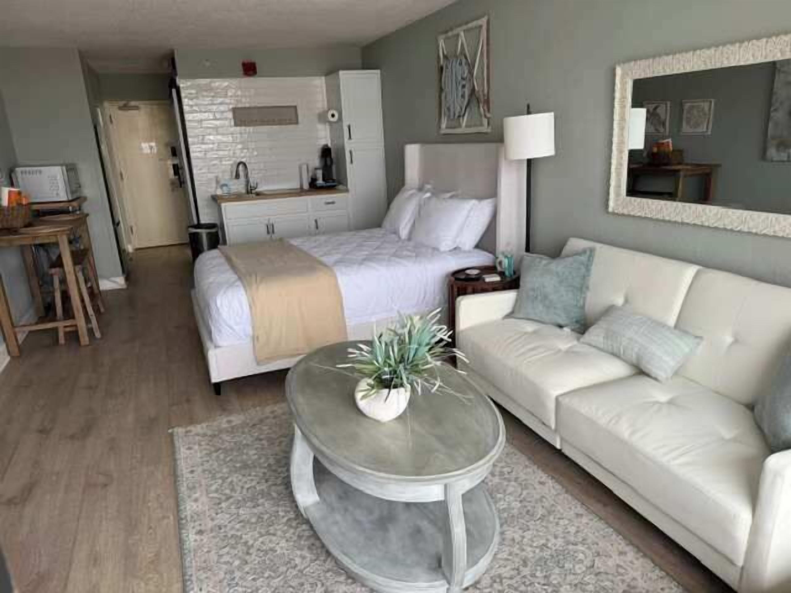 A bedroom with a bed, bedside table, lamp, and a mirror on the wall.