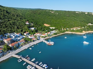 Un poble costaner amb un port esportiu, cases i un paisatge amb turons al fons.