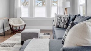 En stue med en grå sofa, en hvid stol, en lampe og et vindue med persienner.