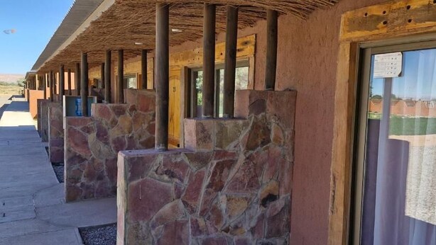 A row of rooms with stone pillars, wooden beams, and large windows with curtains. - Eltoconar atacama (San Pedro de Atacama)