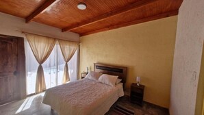 A bedroom with a wooden ceiling, a bed with a headboard, a nightstand, and a window with curtains. - Eltoconar atacama (San Pedro de Atacama)