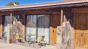 A building with a stone facade, wooden doors, and a patio area with chairs and a table. - Eltoconar atacama (San Pedro de Atacama)