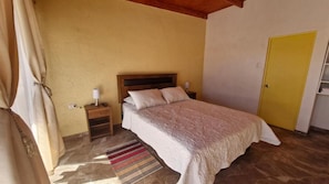 A bedroom with a bed, nightstands, a yellow door, and a striped rug. - Eltoconar atacama (San Pedro de Atacama)
