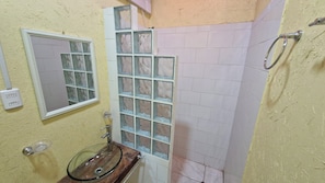 A bathroom with a glass sink, a window with frosted glass, and a shower area.