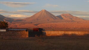 A mountain landscape with a prominent peak, a small building, and a clear sky. - Eltoconar atacama (San Pedro de Atacama)