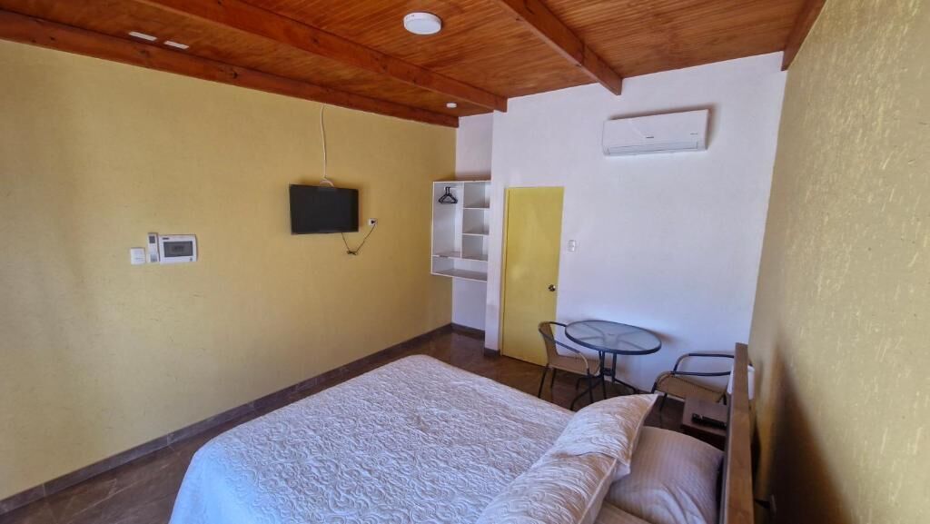 A bedroom with a bed, a small table, a chair, a TV, and a wardrobe.
