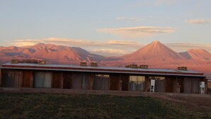 A single-story building with a flat roof, multiple windows, and a door. - Eltoconar atacama (San Pedro de Atacama)