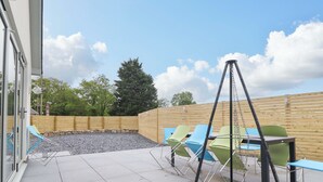 Un patio exterior con una silla colgante, una parrilla y sillas azules.