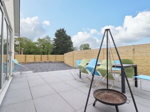 An outdoor patio with a swing chair, a grill, and blue chairs. - Kingfisher (Llanbedr)