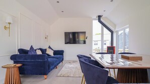 Una sala moderna con un sofá azul, una mesita de madera, un ventanal grande y una zona de comedor con una mesa y sillas de madera.