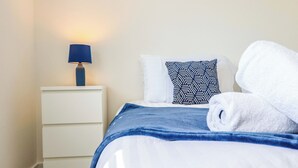 Una cama bien hecha con un edredón azul y una almohada blanca con un diseño geométrico.