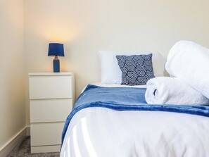 A neatly made bed with a blue blanket and a white pillow with a geometric pattern. - Kingfisher (Llanbedr)