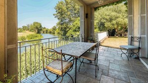 Un patio techado con una mesa y sillas, con vista a un río y follaje.