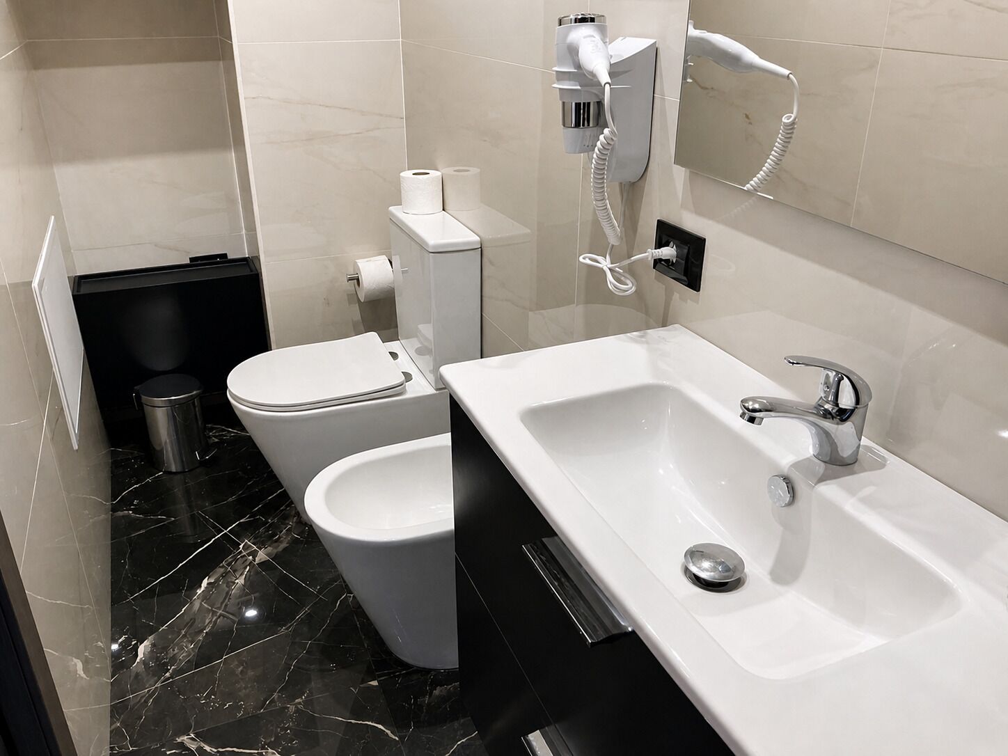 A modern bathroom with a white sink, a bidet, and a toilet.