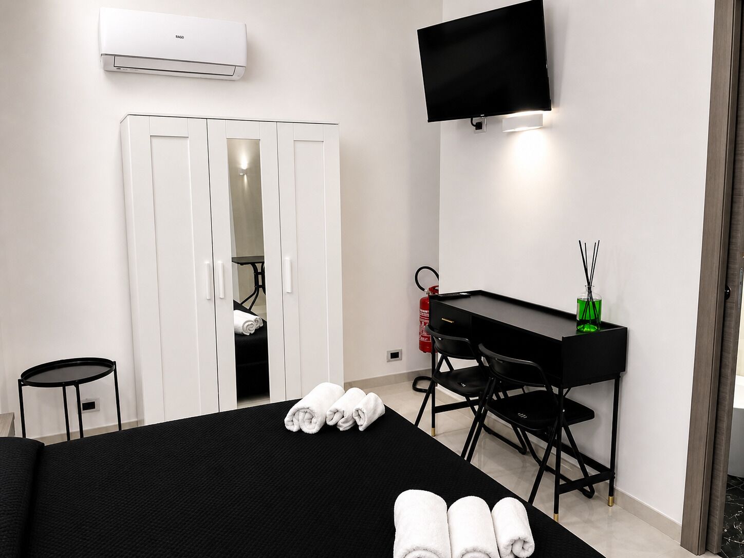 A hotel room with a bed, a desk, a chair, a TV, and a wardrobe.