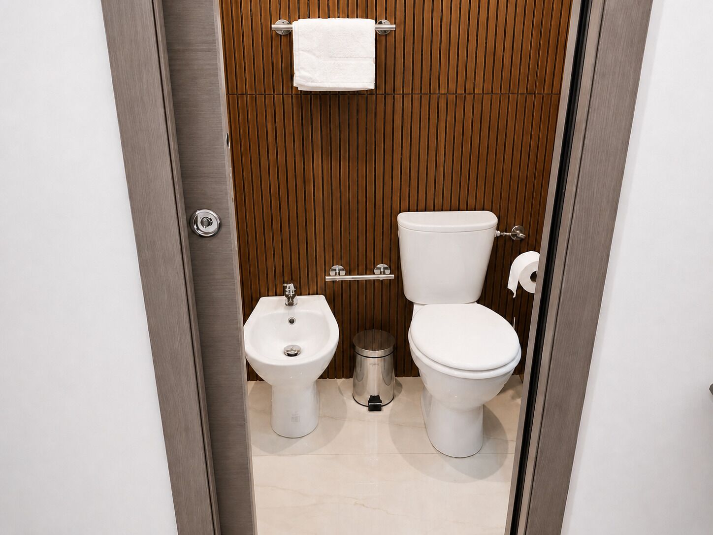 Et moderne badeværelse med bidét, toilet og håndklædestang.