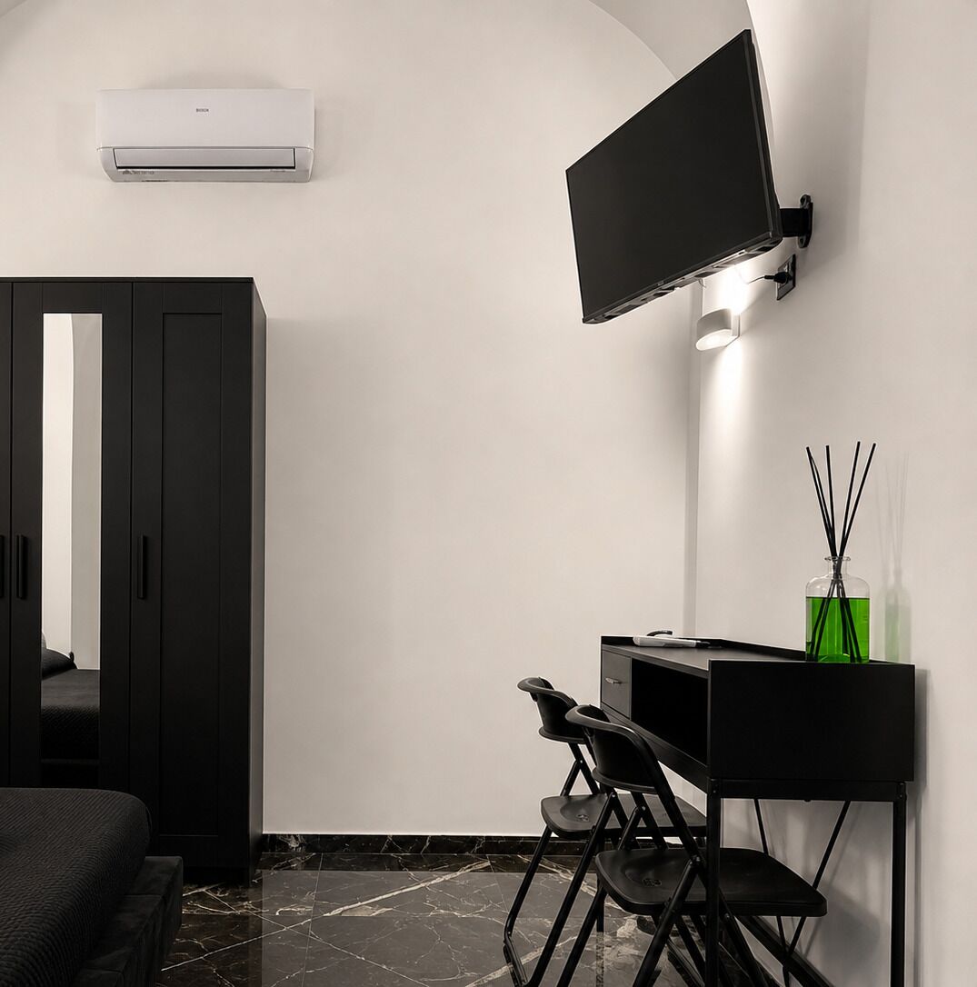 Ein modernes Hotelzimmer mit Flachbildfernseher an der Wand, einem Schreibtisch mit Stuhl und einem Kleiderschrank.