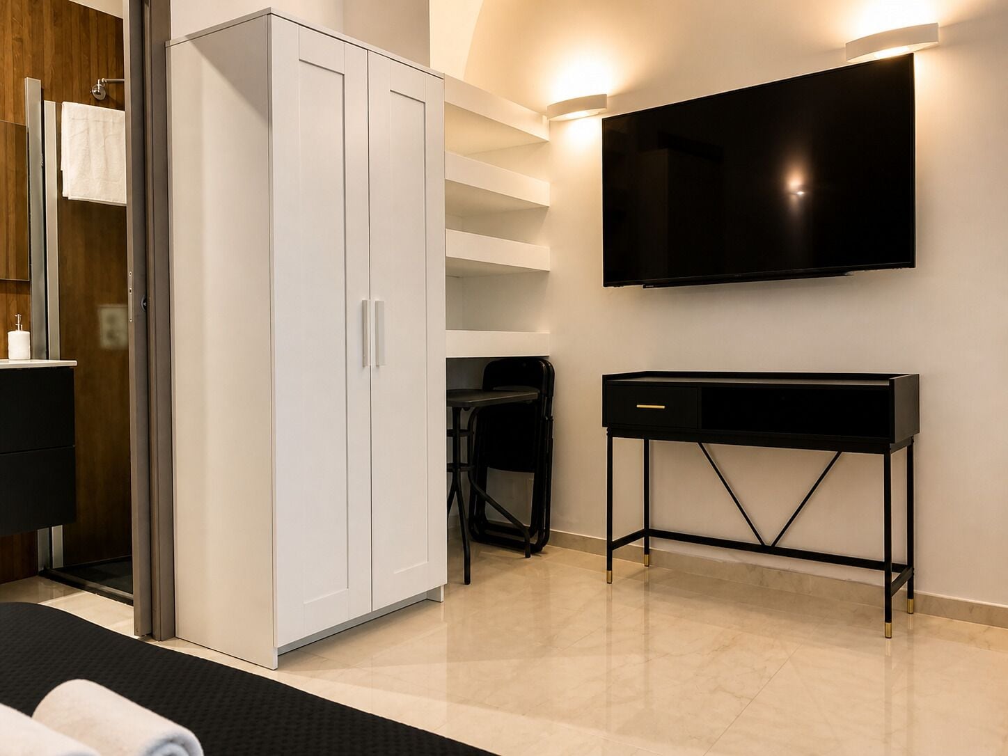 A modern hotel room with a wardrobe, a desk, a flat-screen TV, and a shower area.
