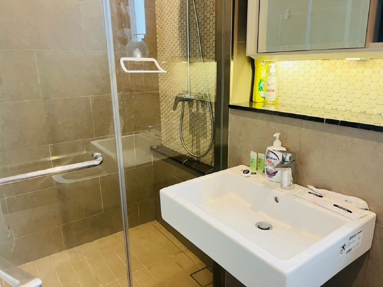 Et badeværelse med et glasbrusekabine, en hvid vask med toiletartikler og et spejl over vasken.