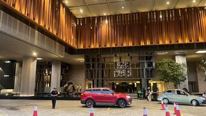 A modern building entrance with a red SUV parked in front, a security guard, and a few people entering. - Luxury Suite Lucentia BBCC Infinity Pool (Kuala Lumpur)