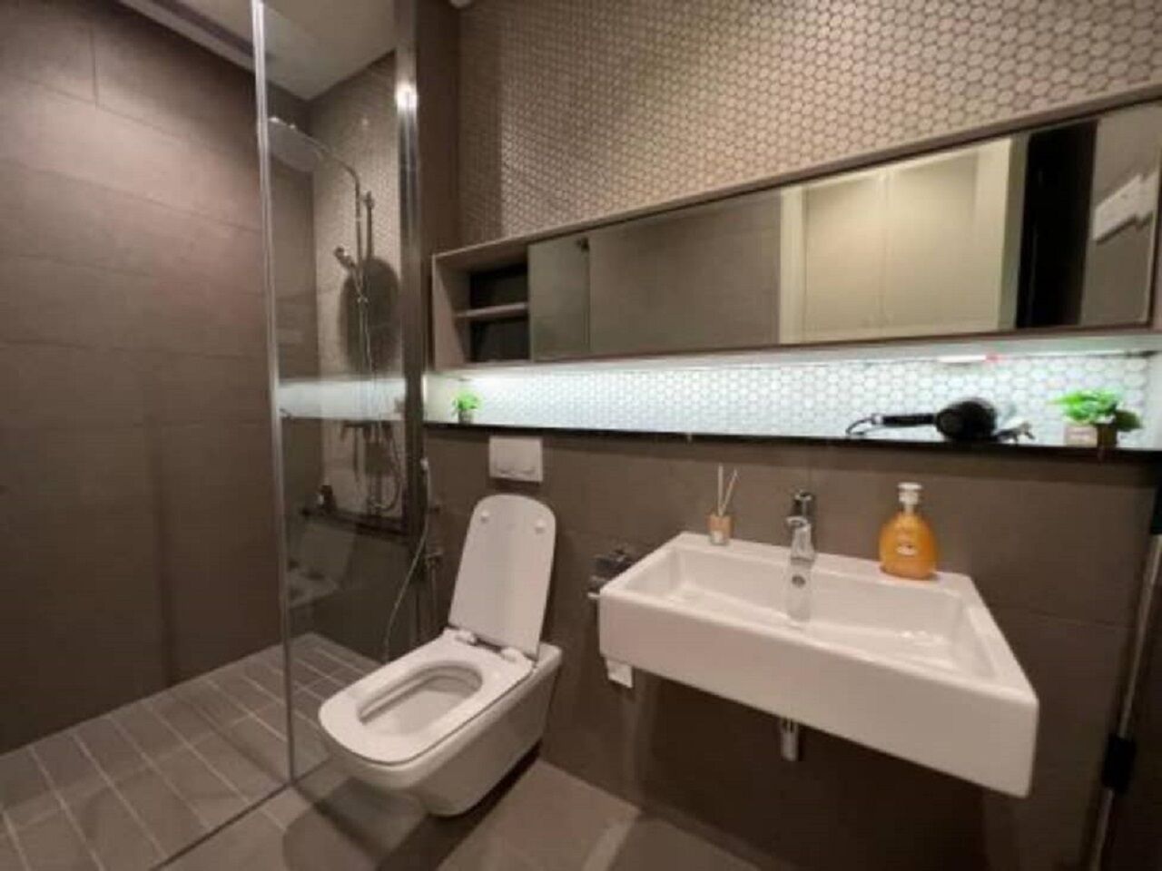 Un baño moderno con ducha de vidrio, inodoro blanco y lavamanos con espejo.