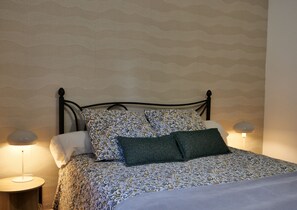 Cama bem arrumada com roupa de cama estampada, duas luminárias de cabeceira e parede com textura.