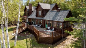 Una cabaña de troncos con terraza, mobiliario exterior y una chimenea.