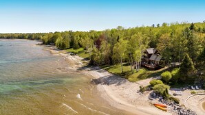 Una cabaña junto al lago con terraza, rodeada de árboles y una playa de arena.