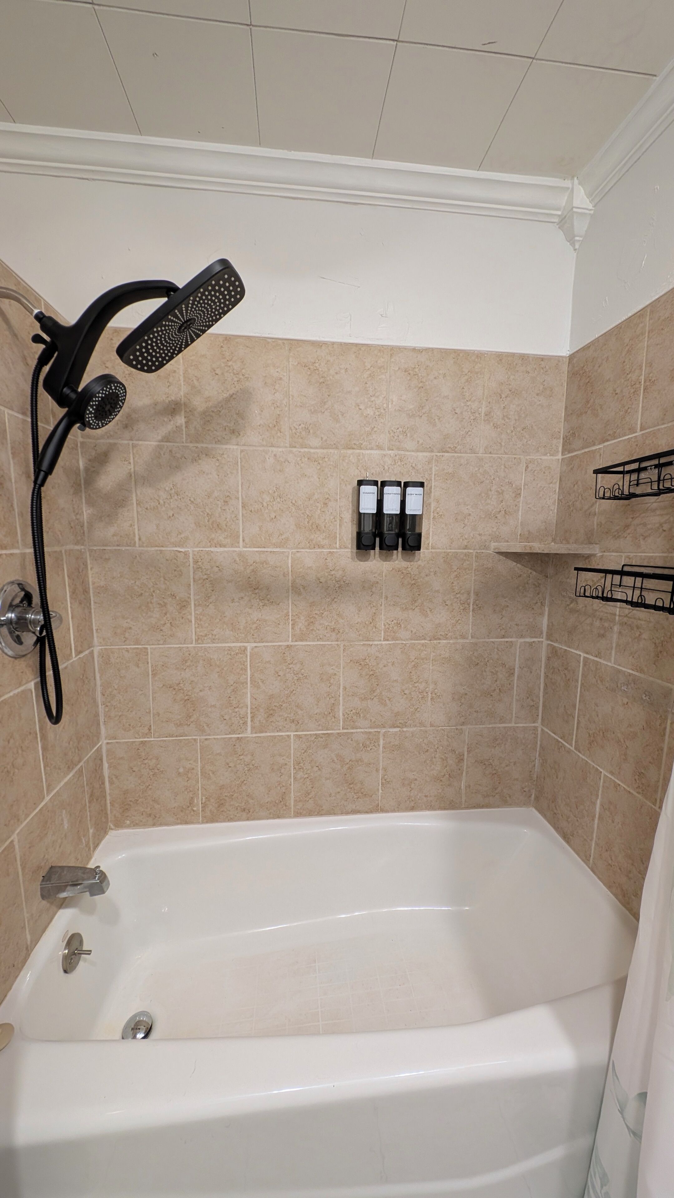 Une salle de bain équipée d’une baignoire, d’un pommeau de douche à main et d’un distributeur de savon mural.