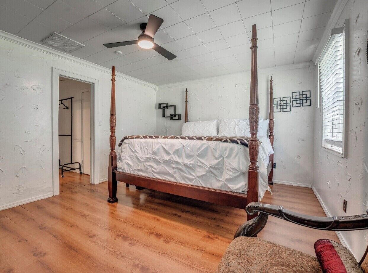 Una cama con dosel en una habitación con suelo de madera, ventilador de techo y ventana con persianas.