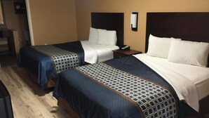 A hotel room with two beds, each with a patterned bedspread, a nightstand, and a wall-mounted mirror. - Crossroads Hotel and Suites Irving (Irving)