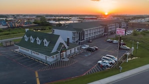 A hotel with a parking lot, a sign for 'Crossroads Hotel,' and a sunset in the background. - Crossroads Hotel and Suites Irving (Irving)