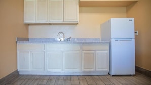 A kitchen with white cabinets, a sink, and a white refrigerator. - Crossroads Hotel and Suites Irving (Irving)